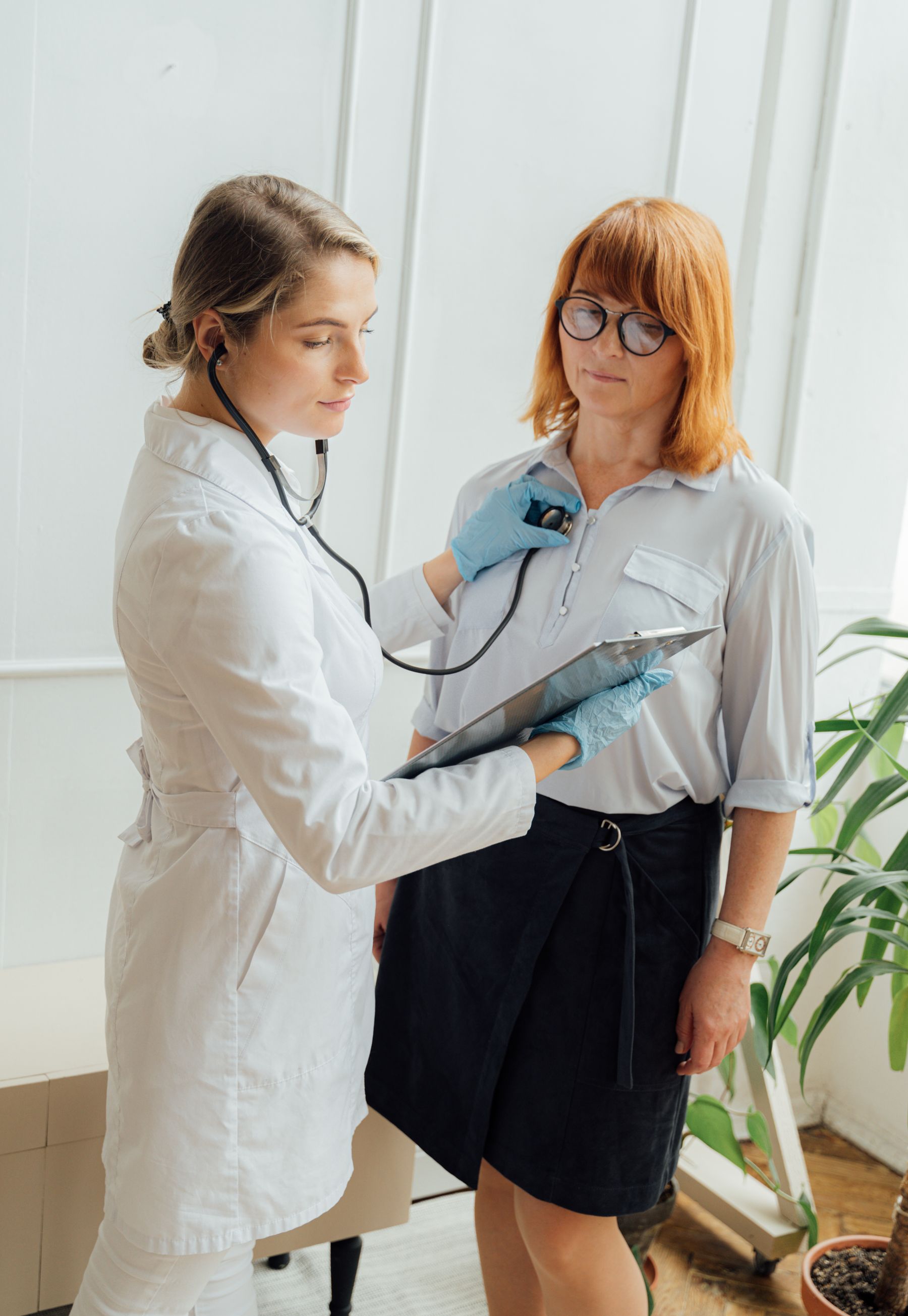 Mulher em consulta com médica de jaleco branco, num consultório luminoso e sereno.